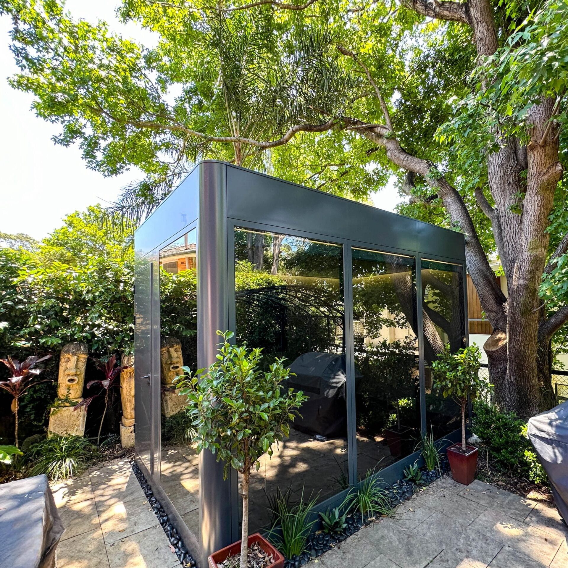 Backyard office Lane cove Compact modular garden pod with dark frame and glass walls under a large tree
