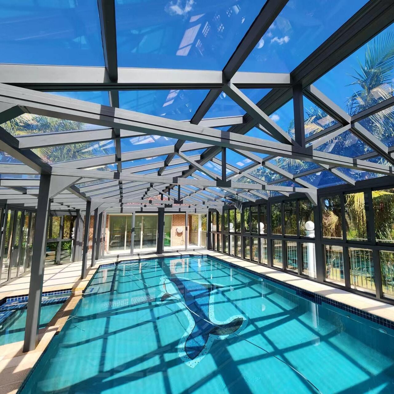 Pool_enclosure Glass pool enclosure with clear roof and black frame surrounded by palm trees